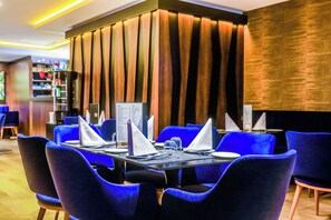 A restaurant with blue chairs, a black table, and a menu stand. - Sbn Suites Hotel (Tangier)