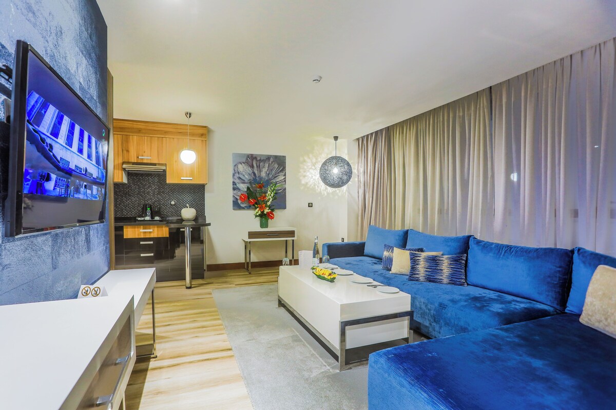 A modern living room with a blue sofa, a white coffee table, and a TV mounted on the wall.