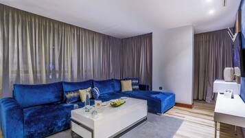 A modern living room with a blue sofa, a white coffee table, and a grey curtain backdrop.
