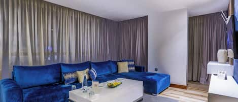 A modern living room with a blue sofa, a white coffee table, and a grey curtain backdrop.