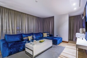 A modern living room with a blue sofa, a white coffee table, and a grey curtain backdrop. - Sbn Suites Hotel (Tangier)