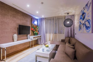 A modern living room with a sofa, a TV mounted on the wall, a long white table, and a decorative vase. - Sbn Suites Hotel (Tangier)