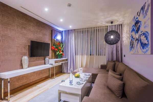 A modern living room with a sofa, a TV mounted on the wall, a long white table, and a decorative vase. - Sbn Suites Hotel (Tangier)
