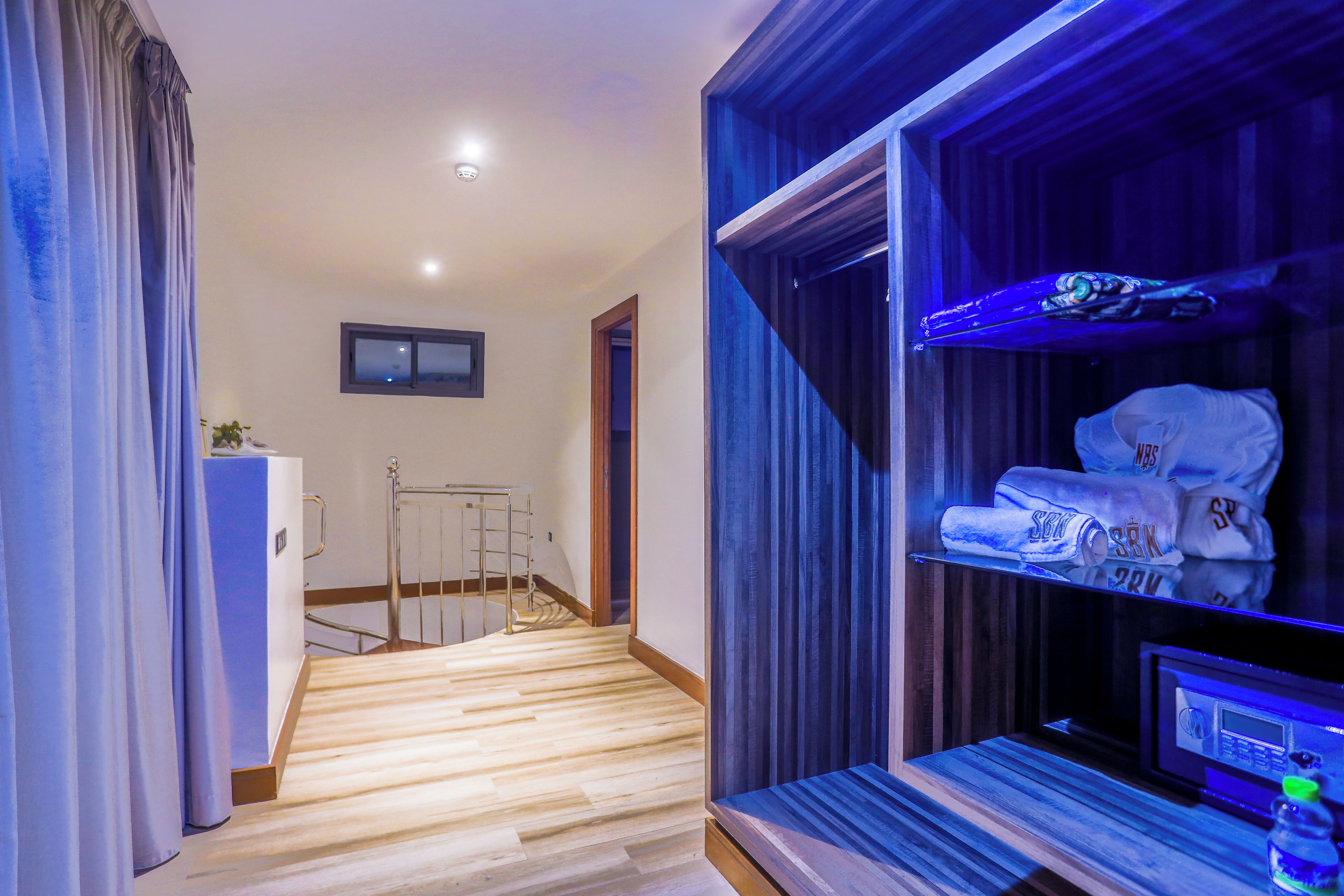 A hotel room with a wooden floor, a bed, a TV, and a shelf with towels.