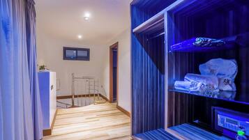 A hotel room with a wooden floor, a bed, a TV, and a shelf with towels.
