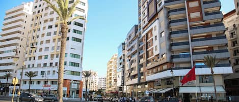 A multi-story hotel with balconies, a flag, and a street in front.