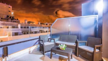 A rooftop terrace with wicker furniture and a glass partition.