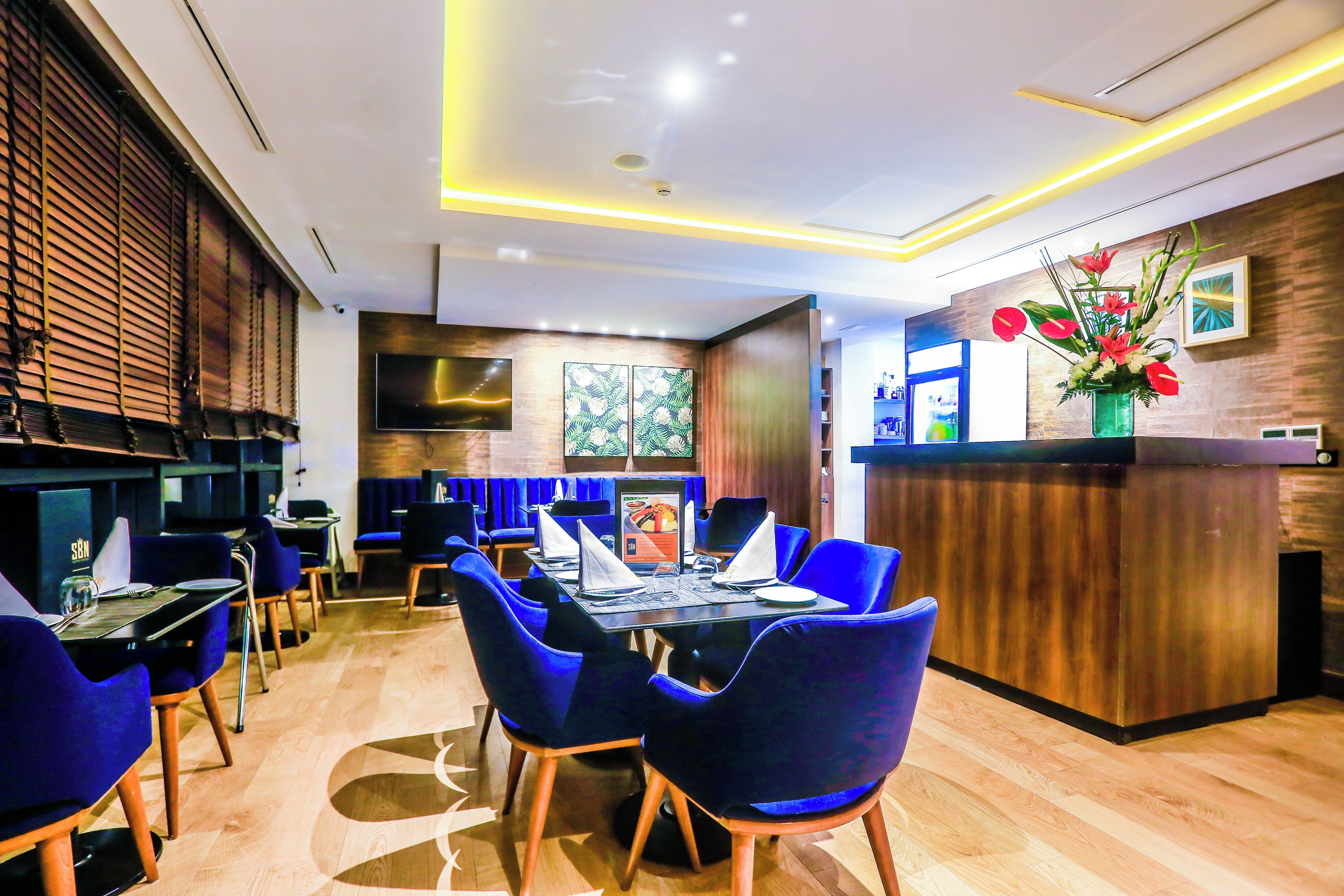 A modern restaurant with a wooden floor, blue upholstered chairs, and a central dining table.