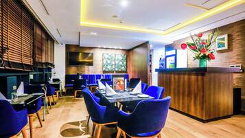 A modern restaurant with a wooden floor, blue upholstered chairs, and a central dining table.