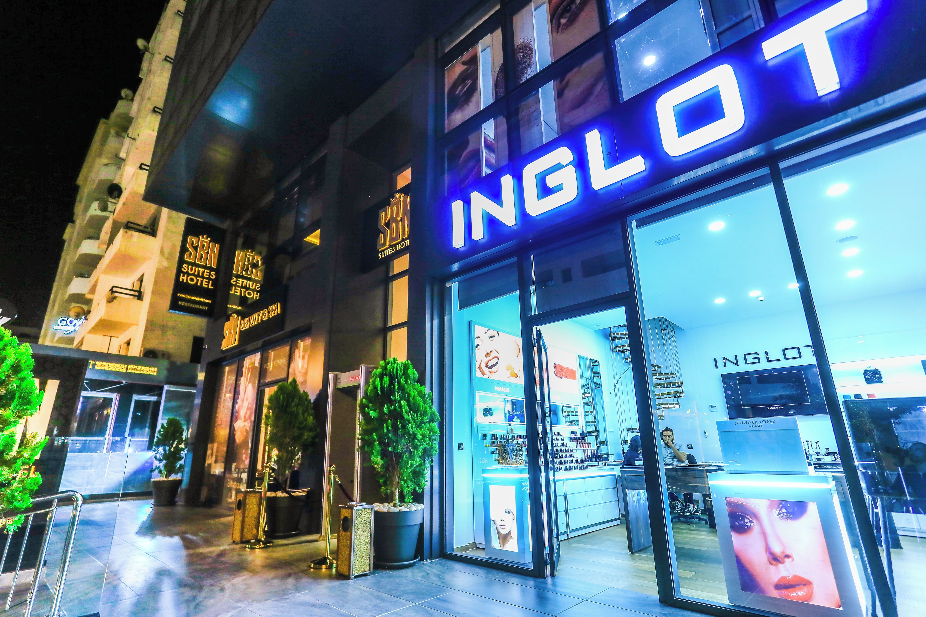 A hotel entrance with a prominent 'INGLOT' sign, a glass facade, and a visible interior with a reception desk and display cases.