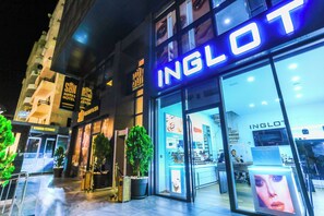 A hotel entrance with a prominent 'INGLOT' sign, a glass facade, and a visible interior with a reception desk and display cases. - Sbn Suites Hotel (Tangier)