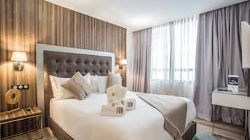 A modern hotel room with a large bed, wooden panel walls, and a view of the city through large windows.