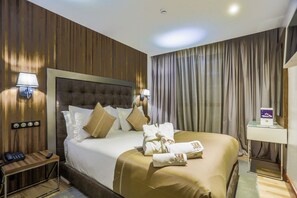 A hotel room with a large bed, a bedside table with a lamp, a nightstand with a phone, and a wall-mounted clock. - Sbn Suites Hotel (Tangier)