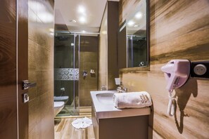 A modern bathroom with a glass shower enclosure, a sink with a towel, and a hairdryer mounted on the wall. - Sbn Suites Hotel (Tangier)