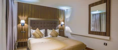 Ein Hotelzimmer mit einem großen Bett, zwei Nachttischlampen, einem Kopfteil, einem Spiegel und Vorhängen.