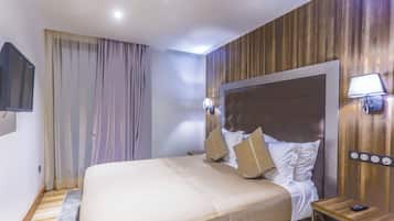 A hotel room with a large bed, wooden paneling on the walls, a mounted TV, and a bedside table with a lamp.