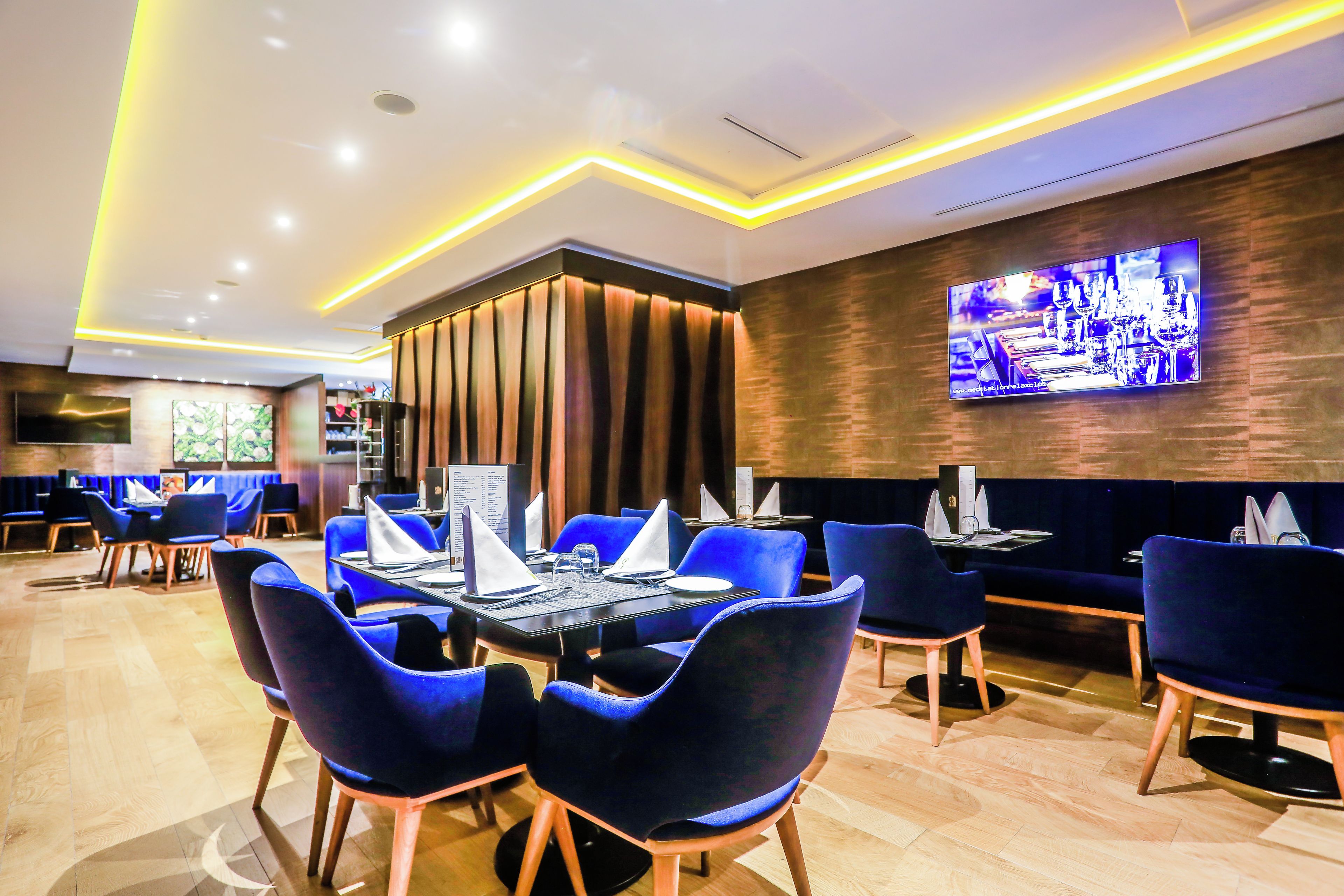 Un restaurante con sillas azules, mesas de madera y un televisor en la pared.