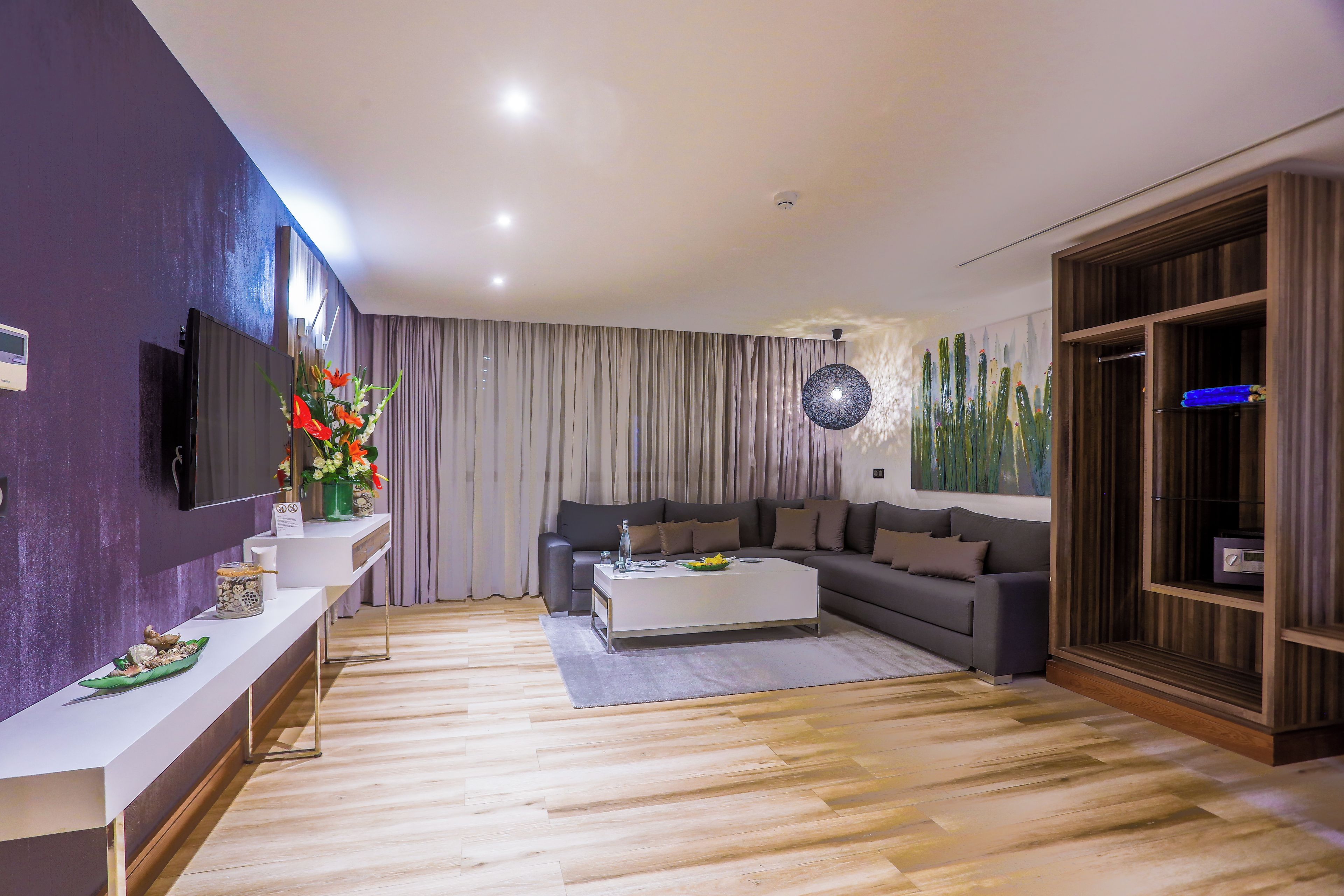 A modern living room with a flat-screen TV, a white coffee table, a grey sofa, and a wooden cabinet.