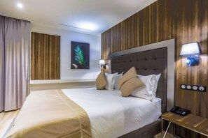 A hotel room with a large bed, a bedside table with a lamp, a wall-mounted power outlet, and a framed leaf artwork. - Sbn Suites Hotel (Tangier)