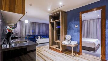 A modern hotel room with a wooden vanity, a bed, a small table, and a large mirror.