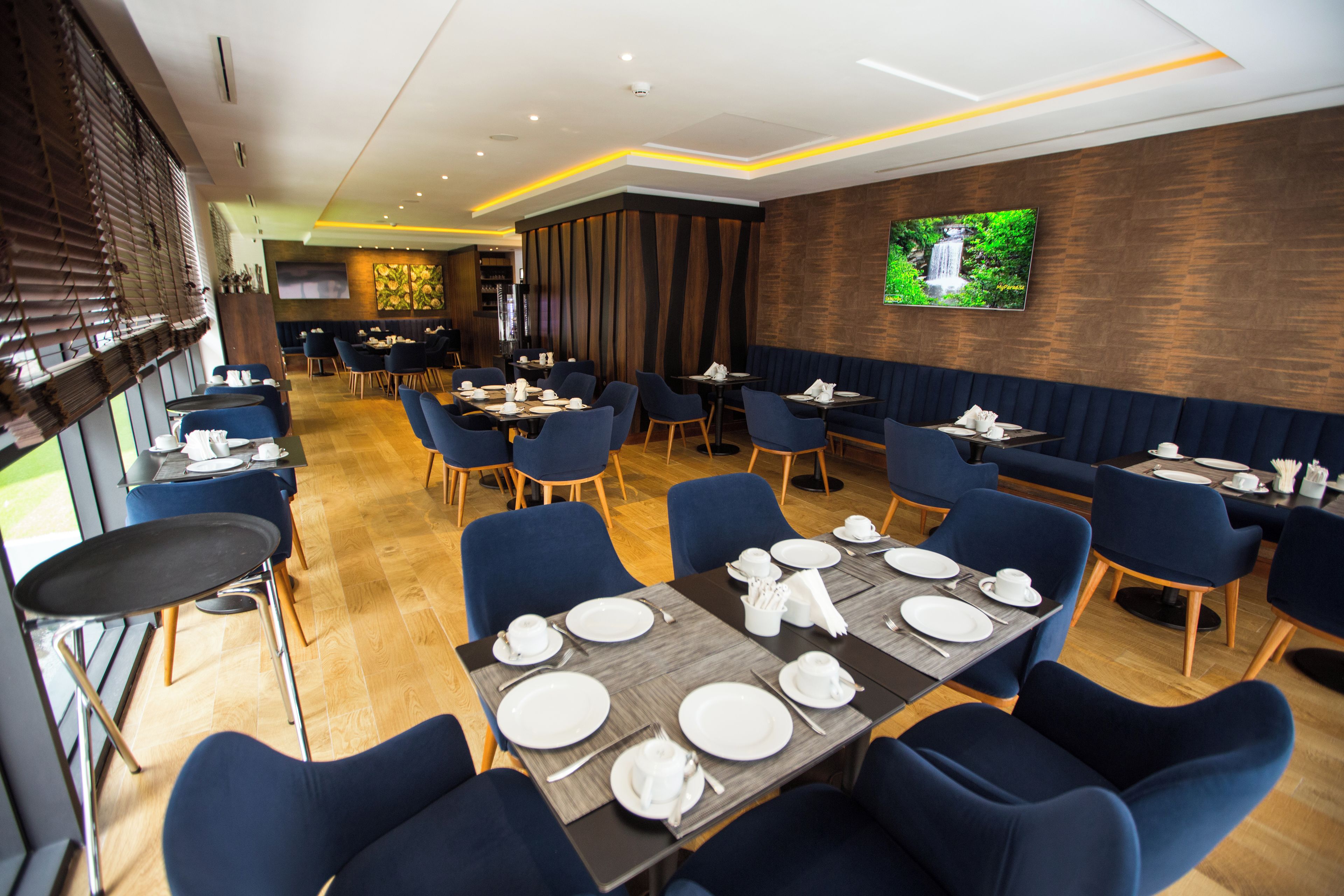 A restaurant with tables set for dining, blue chairs, and a TV on the wall.