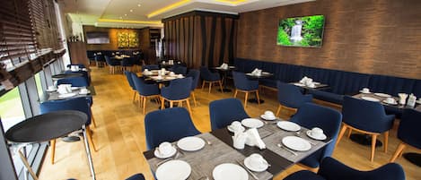 Een restaurant met gedekte tafels, blauwe stoelen en een televisie aan de muur.