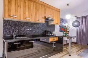 A modern kitchen with wooden cabinets, a black tiled backsplash, and stainless steel appliances. - Sbn Suites Hotel (Tangier)