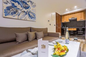 A modern hotel room with a brown sofa, a dining table set with a plate of food, a water bottle, and a menu sign. - Sbn Suites Hotel (Tangier)
