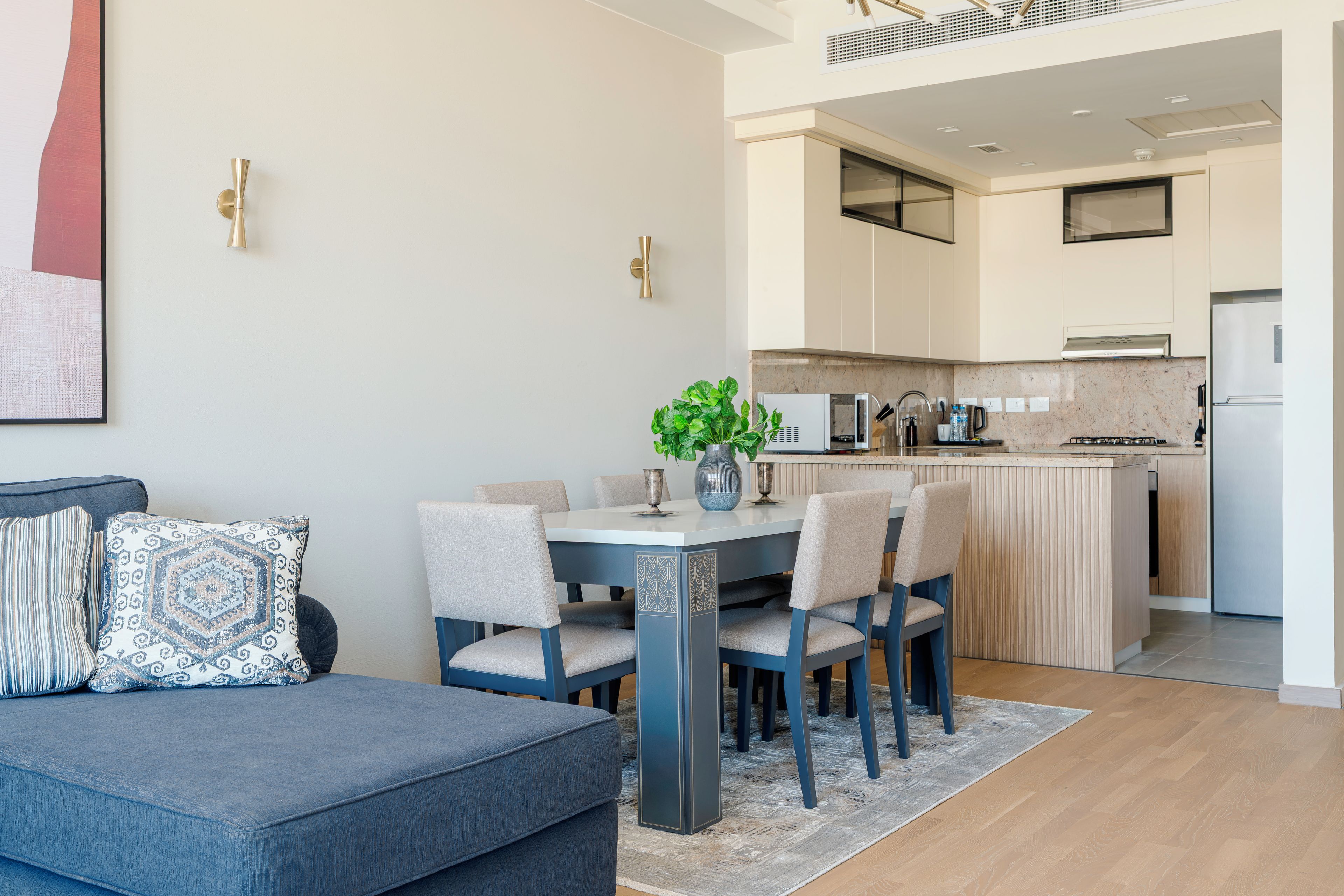A modern living room with a blue sofa, a dining table with chairs, and a kitchen area with a stove and refrigerator.