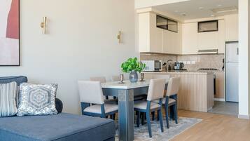 A modern living room with a blue sofa, a dining table with chairs, and a kitchen area with a stove and refrigerator.