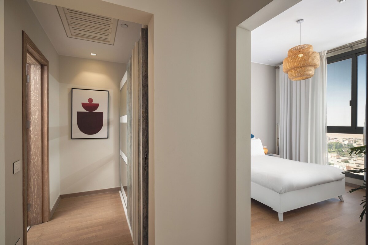 Un dormitorio moderno con una cama, un ventanal con cortinas y una lámpara colgante.