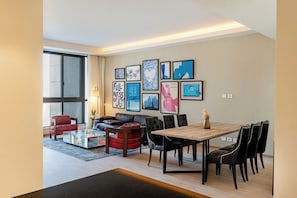 Una sala de estar moderna con comedor, ventanas amplias y varias obras de arte enmarcadas en las paredes.