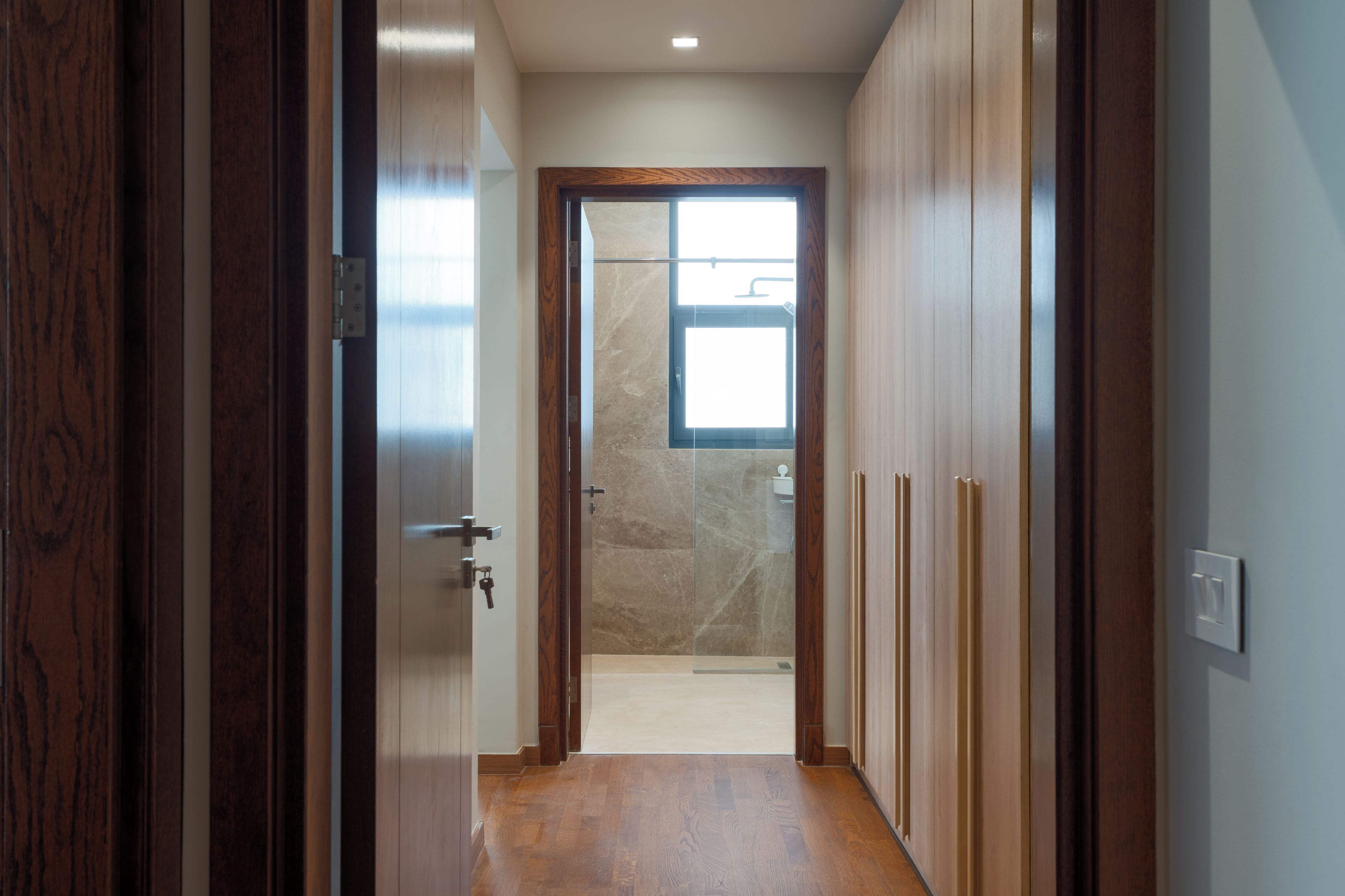 A hallway leading to a bathroom with a glass shower door and a wooden door frame.