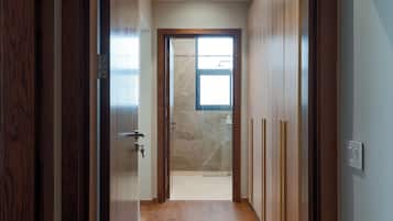 A hallway leading to a bathroom with a glass shower door and a wooden door frame.