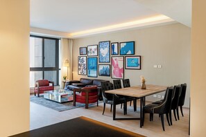 Una sala de estar moderna con comedor, ventanas amplias y varias obras de arte enmarcadas en las paredes.