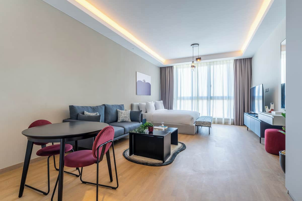 Una habitación de hotel moderna con sofá, una mesa de comedor, televisión y un ventanal con cortinas.
