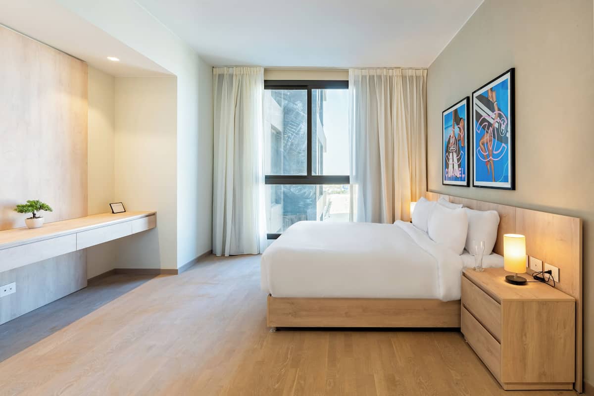 Una habitación de hotel moderna con cama, mesita de noche, lámpara y una obra de arte en la pared.