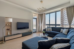 A modern living room with a sectional sofa, a flat-screen TV mounted on the wall, a glass coffee table, and a floor lamp.