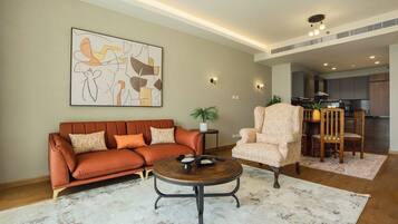 A living room with a sofa, armchair, coffee table, and artwork on the wall.