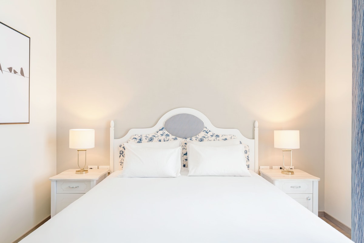 A bed with a white headboard, two bedside tables with lamps, and a wall-mounted artwork.