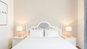 A bed with a white headboard, two bedside tables with lamps, and a wall-mounted artwork.