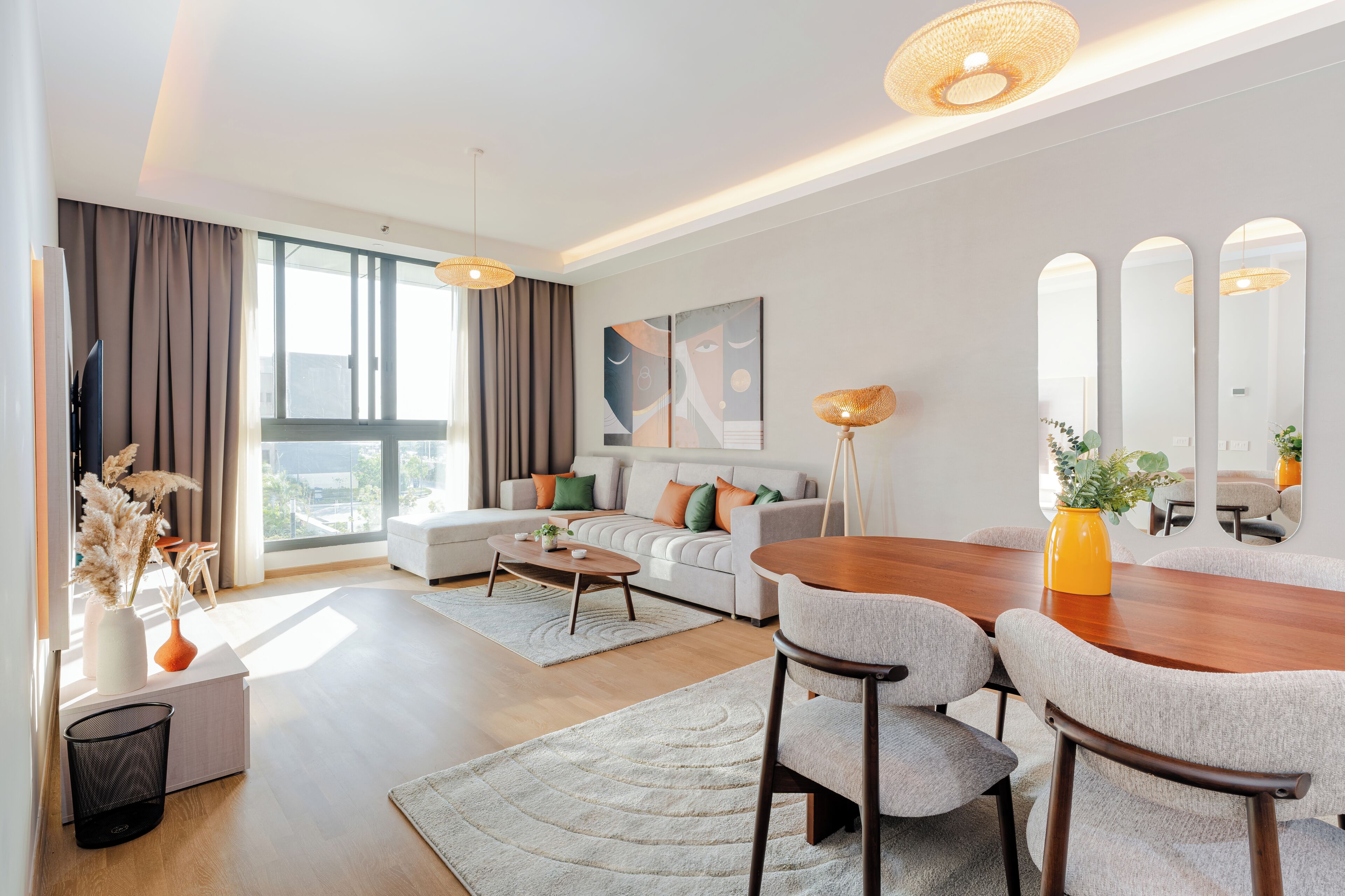 Una sala moderna con un sofá, una mesa de centro, una mesa de comedor y sillas. Hay un ventanal con cortinas, un cuadro en la pared y un espejo.