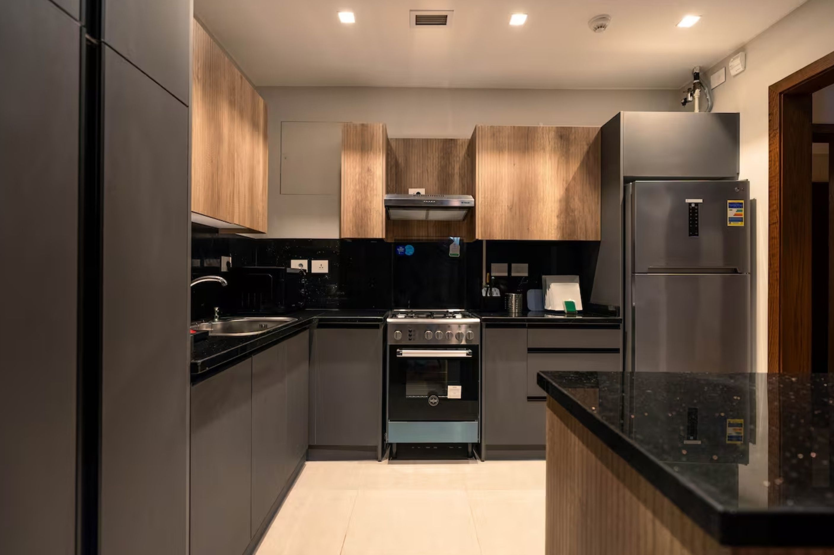 Eine moderne Küche mit dunklen Schränken, einem Edelstahl-Kühlschrank, einem eingebauten Backofen und einem Gasherd.