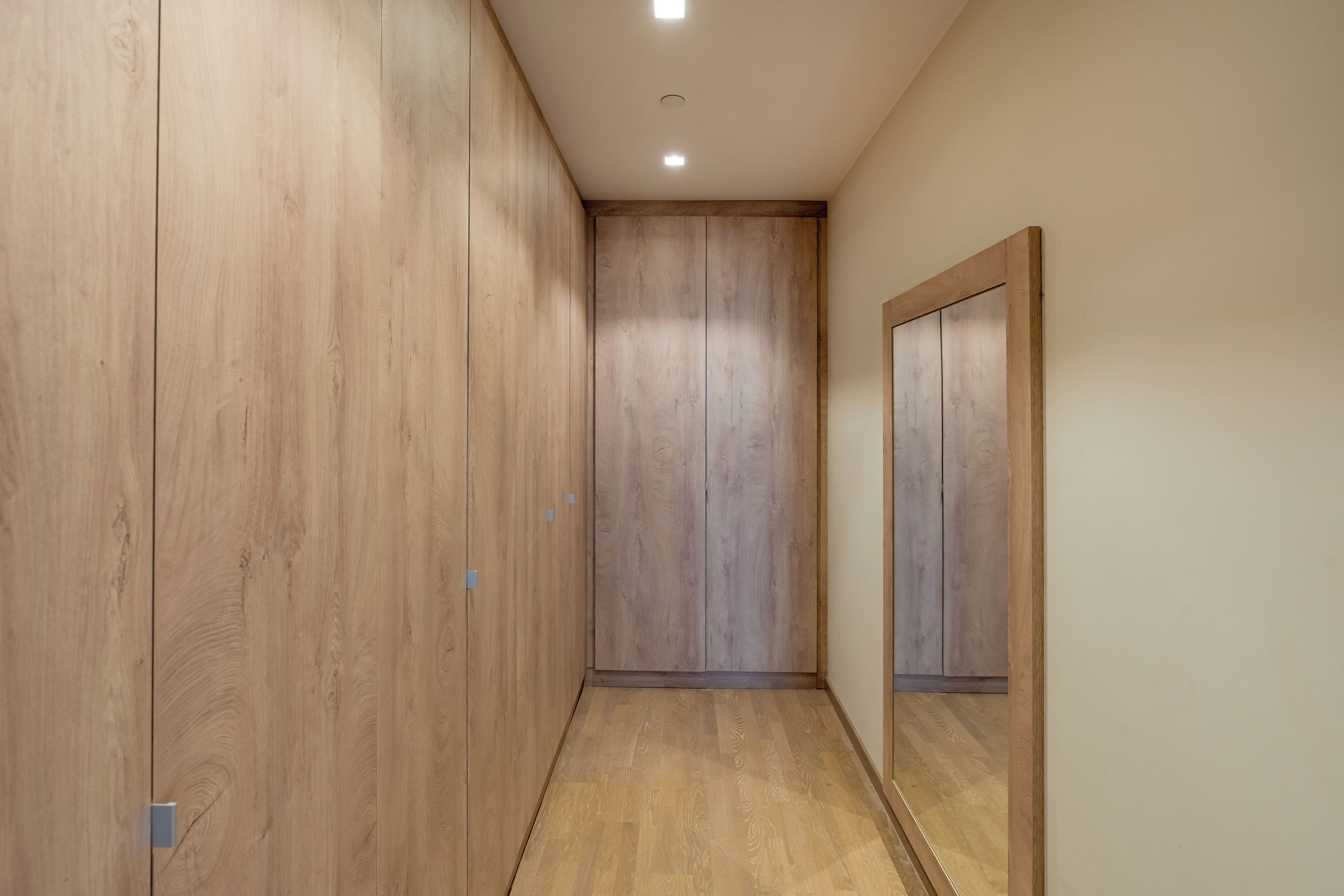 A hallway with wooden flooring and a mirrored wall.