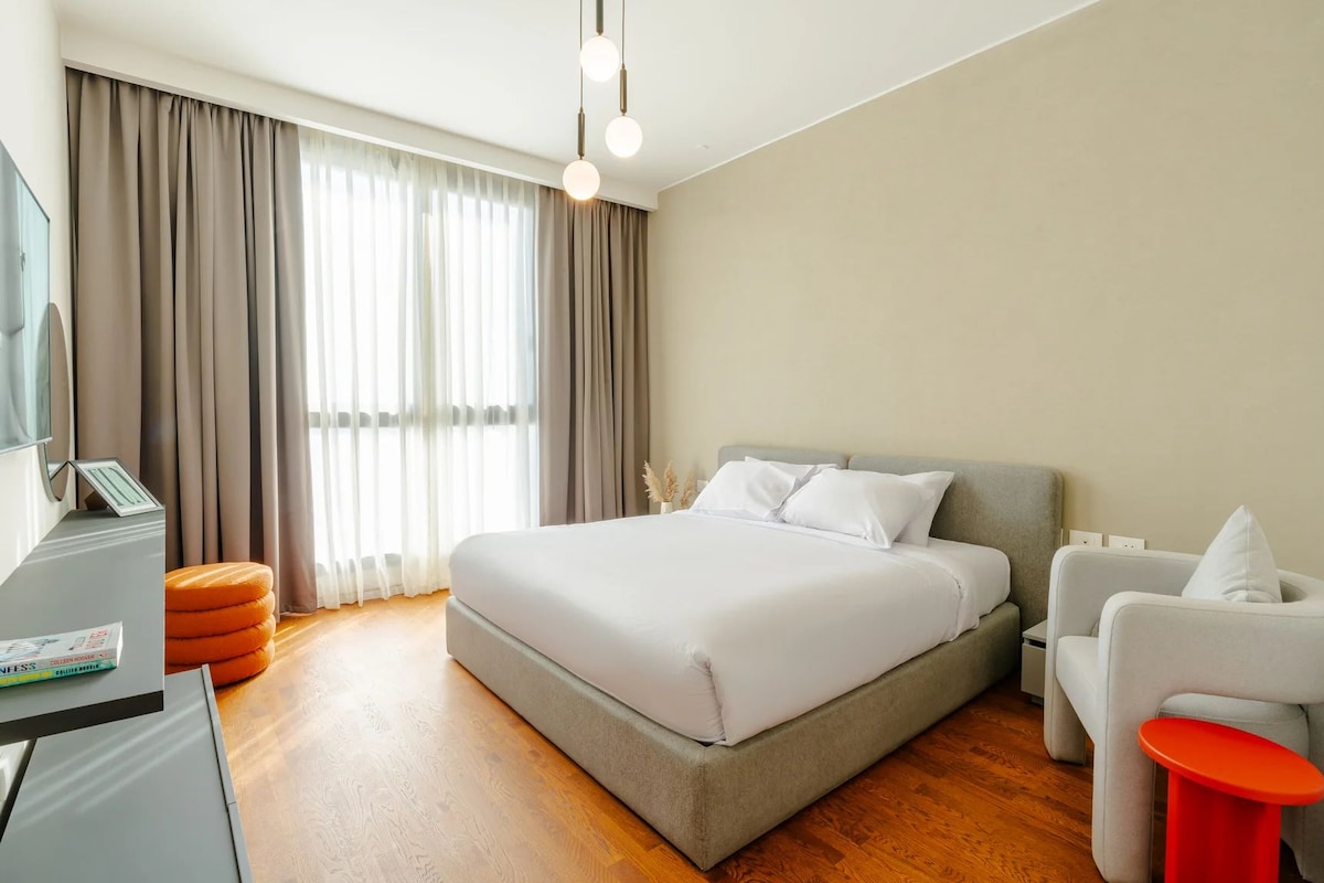 Una habitación de hotel moderna con una cama grande, un escritorio con una computadora, una silla y una mesita.