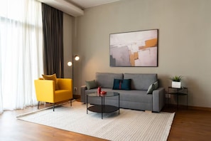 A modern living room with a grey sofa, a yellow armchair, a glass coffee table, and a painting on the wall. - Brassbell Sheikh Zayed Aeon Towers (6th of October City)