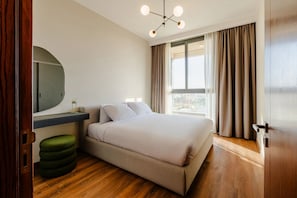 Un dormitorio con una cama, un espejo redondo, una mesita pequeña y una ventana con cortinas.
