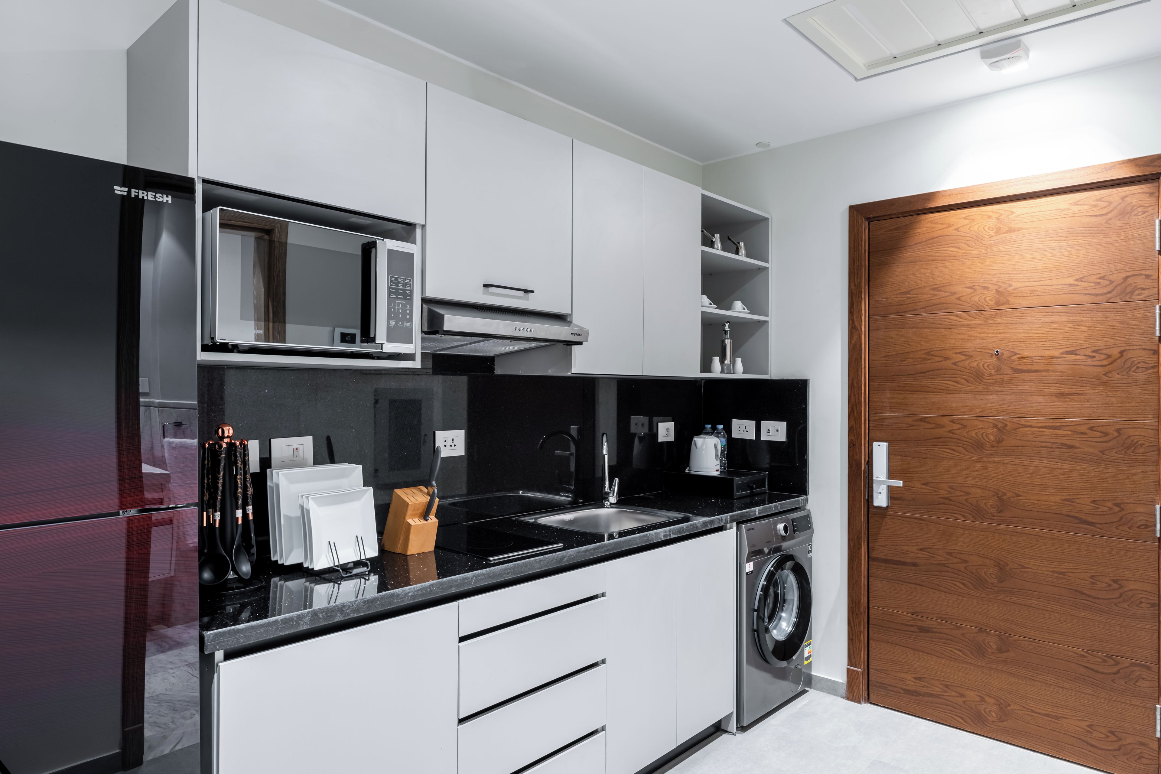 A modern kitchen with a refrigerator, microwave, stove, sink, and washing machine.