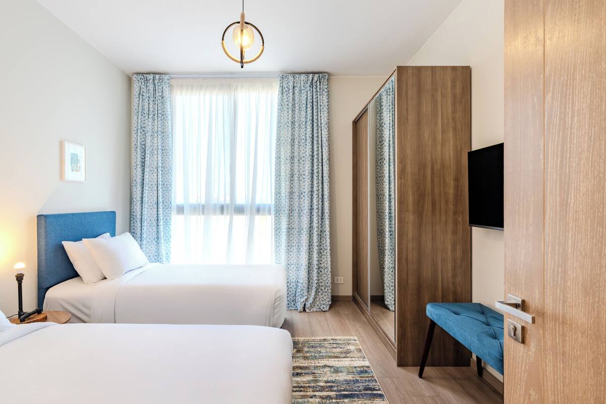 Una habitación de hotel con dos camas, un espejo grande, un televisor y un armario de madera.
