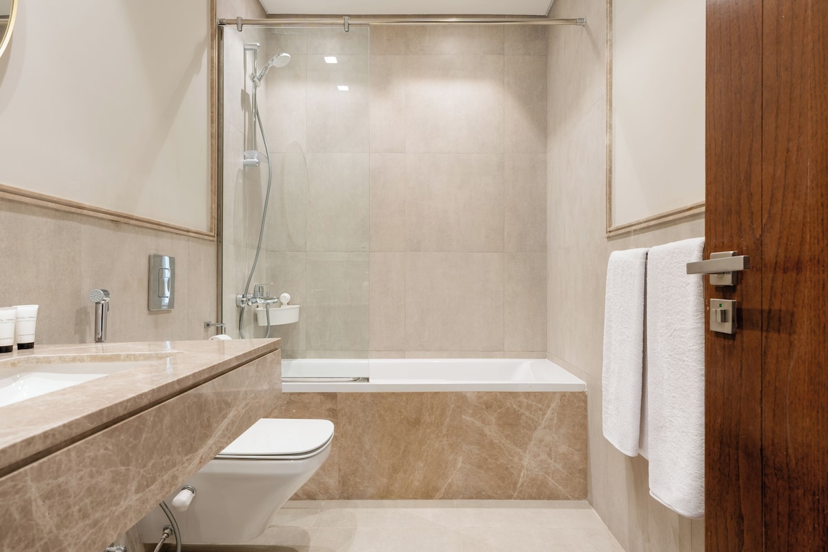 A modern bathroom with a glass-enclosed shower, a white bathtub, and a vanity with a sink and mirror.